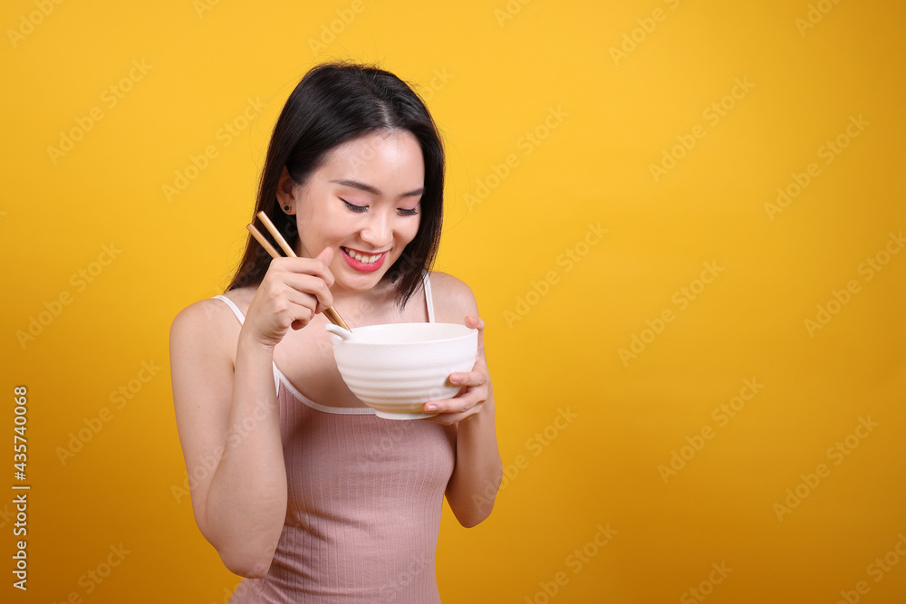 Beautiful young south east Asian woman holding chines empty chopstick Chinese soup spoon bowl utensil pretend acting posing see eat taste smell feed offer satisfaction yummy yellow orange background Beautiful young south east Asian woman holding chines empty chopstick Chinese soup spoon bowl utensil pretend acting posing see eat taste smell feed offer satisfaction yummy yellow orange background