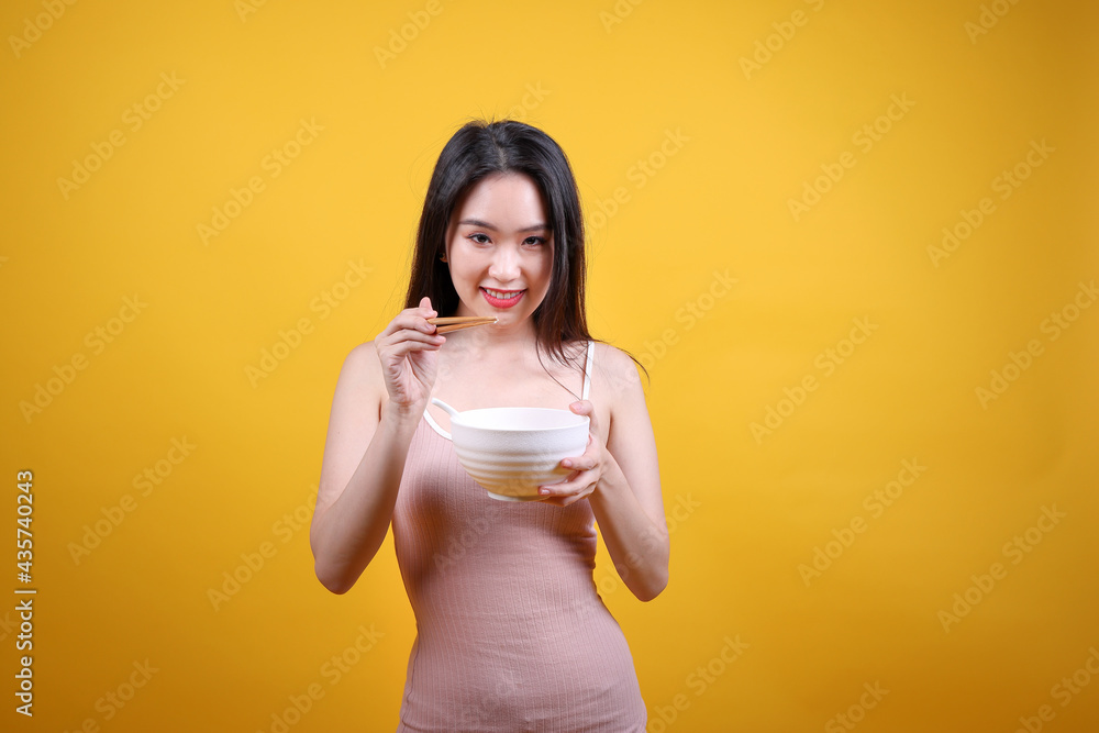 Beautiful young south east Asian woman holding chines empty chopstick Chinese soup spoon bowl utensil pretend acting posing see eat taste smell feed offer satisfaction yummy yellow orange background Beautiful young south east Asian woman holding chines empty chopstick Chinese soup spoon bowl utensil pretend acting posing see eat taste smell feed offer satisfaction yummy yellow orange background