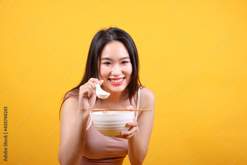 Beautiful young south east Asian woman holding chines empty chopstick Chinese soup spoon bowl utensil pretend acting posing see eat taste smell feed offer satisfaction yummy yellow orange background Beautiful young south east Asian woman holding chines empty chopstick Chinese soup spoon bowl utensil pretend acting posing see eat taste smell feed offer satisfaction yummy yellow orange background