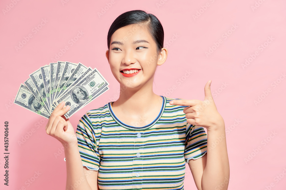 Photo of rich woman in basic clothing holding fan of dollar money isolated over pink background Photo of rich woman in basic clothing holding fan of dollar money isolated over pink background