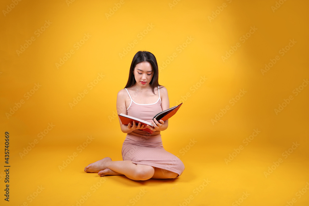 Beautiful young south east Asian woman sit down on floor yellow orange color background read study book magazine pose fashion style elegant beauty mood Beautiful young south east Asian woman sit down on floor yellow orange color background read study book magazine pose fashion style elegant beauty mood