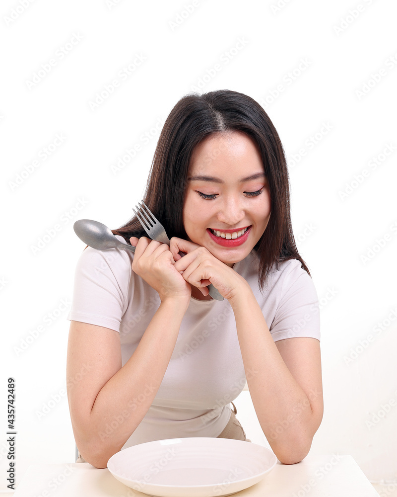 Beautiful young south east Asian woman pretend acting posing holding empty fork spoon in hand eat taste look see white plate on table white background smile happy Beautiful young south east Asian woman pretend acting posing holding empty fork spoon in hand eat taste look see white plate on table white background smile happy