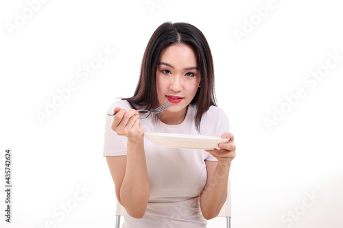 Beautiful young south east Asian woman pretend acting posing holding empty fork spoon in hand eat taste look see white plate on table white background
