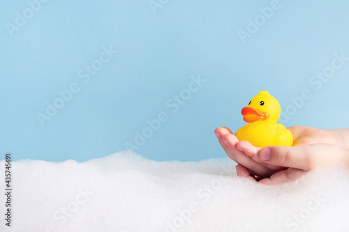 Foto Child hands holding yellow rubber duck in bubble bath on pastel blue background