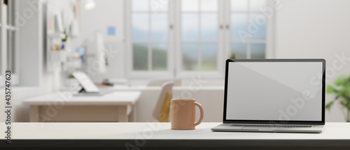 Laptop with mock-up screen and coffee mug on the table in comfortable office room, 3D rendering