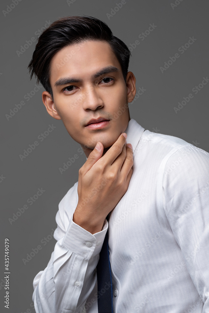 Portrait of smart handsome Asian man in corporate wear touching face in light gray isolated studio background Portrait of smart handsome Asian man in corporate wear touching face in light gray isolated studio background