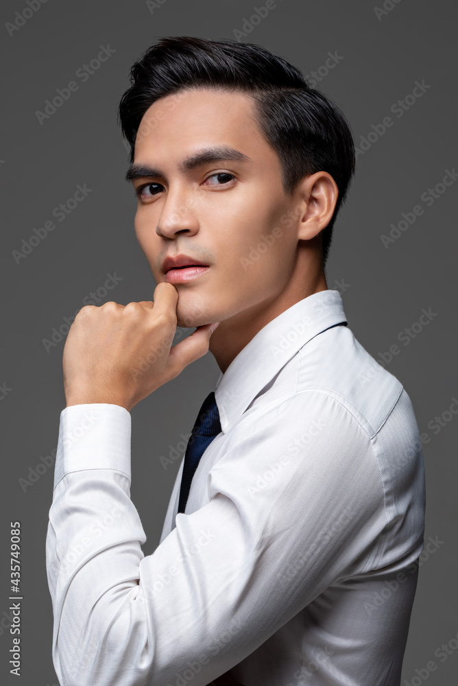 Portrait of smart handsome Asian man in corporate wear touching face in light gray isolated studio background Portrait of smart handsome Asian man in corporate wear touching face in light gray isolated studio background