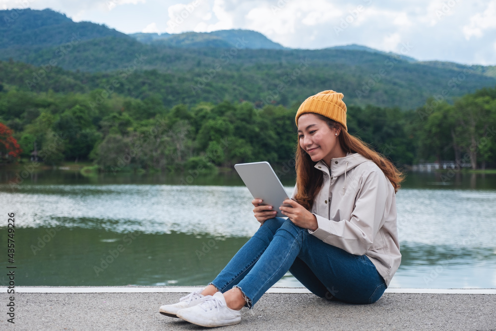 A young woman holding and using digital tablet while traveling mountains and lake