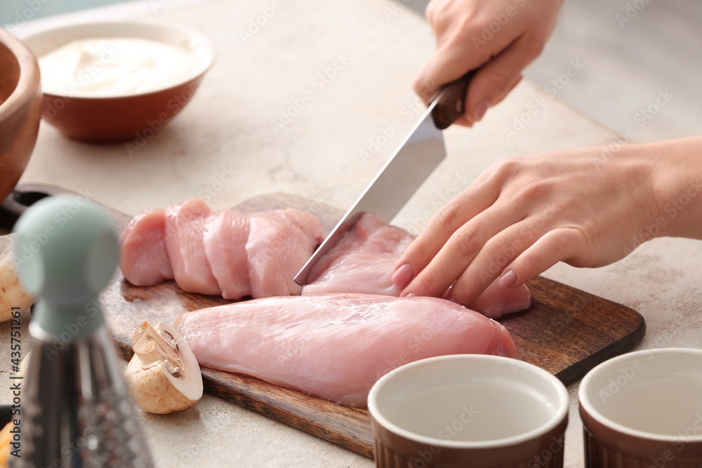 Woman cutting chicken fillet in kitchen, closeup