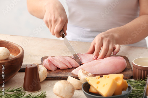 Woman cutting chicken fillet in kitchen