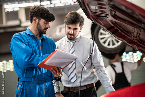 Car service, vehicle repair concept : Car service technician explaining checking list or repaired item to vehicle owner customer after sending car for repairing or check at automobile service center. photo