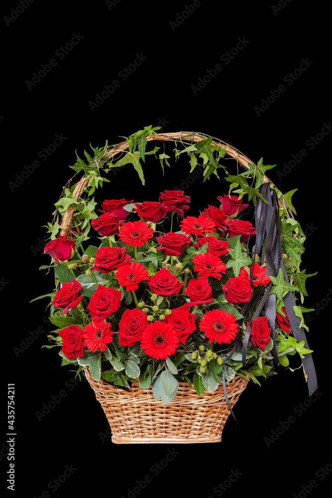 Funeral bouquet of red roses and gerberas in a basket with a black ribbon. Isolated on black background. Vertical. Space for text.