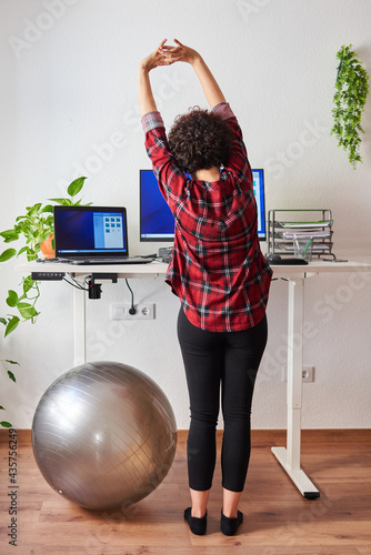 Woman stretches while working at an adjustable desk standing