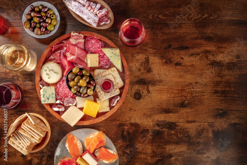Charcuterie and cheese board with wine, overhead flat lay shot on a rustic background with a place for text. Italian antipasti or Spanish tapas, shot from above with olives and salmon sandwiches