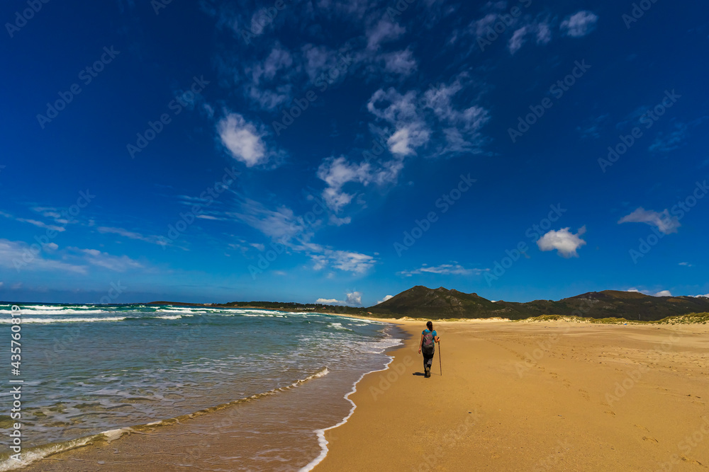 Young woman walk on an empty wild beach towards celestial beams of light falling from the sky Young woman walk on an empty wild beach towards celestial beams of light falling from the sky