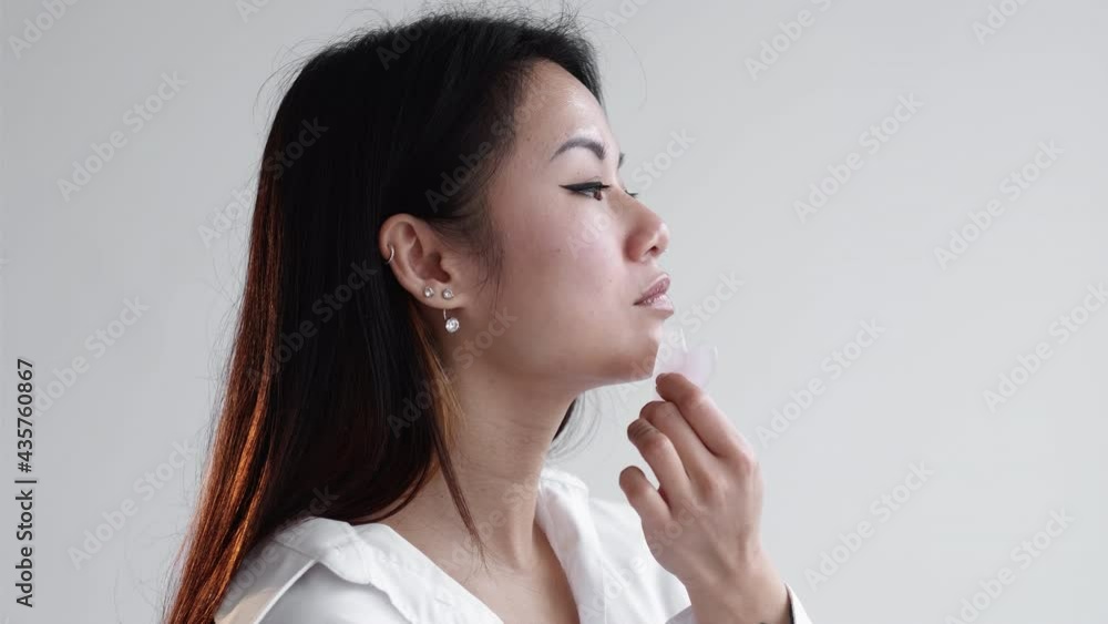 Facial massage. Home beauty procedure. Skin care. Anti-aging treatment. Profile asian woman with stylish tattoo using guasha jade stone on face isolated white copy space. Facial massage. Home beauty procedure. Skin care. Anti-aging treatment. Profile asian woman with stylish tattoo using guasha jade stone on face isolated white copy space.
