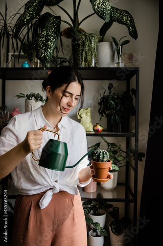 young woman watering a cactus in terracotta pot