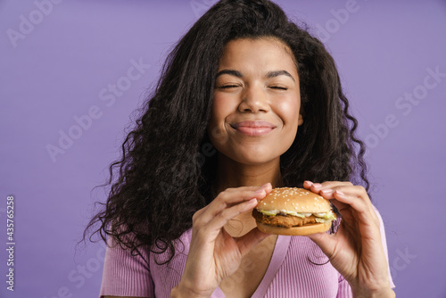 Young black woman with curly hair smiling while eating hamburger