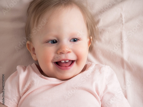 Portrait of a happy laughing baby, with a funny expression on his face. A small beautiful girl with blue eyes smiles cheerfully, the first teeth are visible