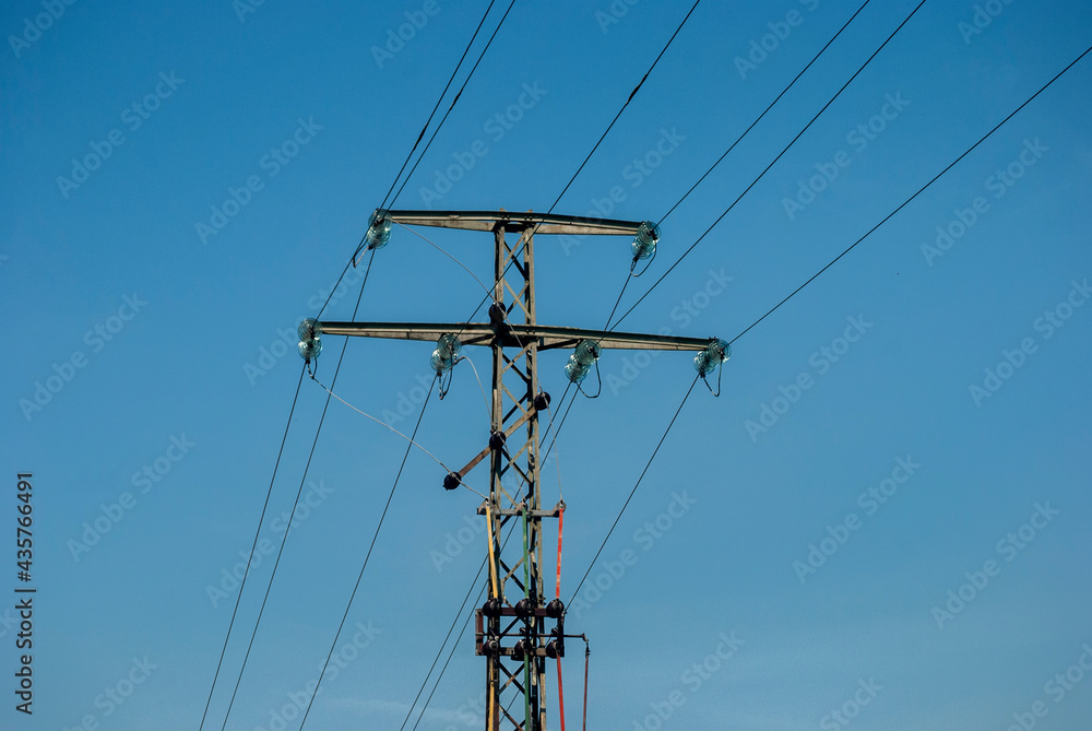 High voltage electric pole and transmission lines on clear blue sky background