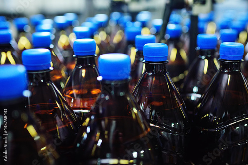 Industrial food production of carbonated beverages  beer  water. Plastic PET bottles with drinks or beer are moving on a conveyor belt in the background of the factory.