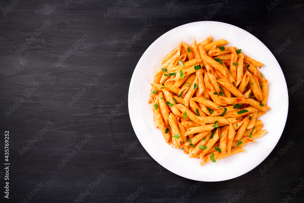 Penne pasta in tomato sauce, decorated with parsley on a black background Penne pasta in tomato sauce, decorated with parsley on a black background