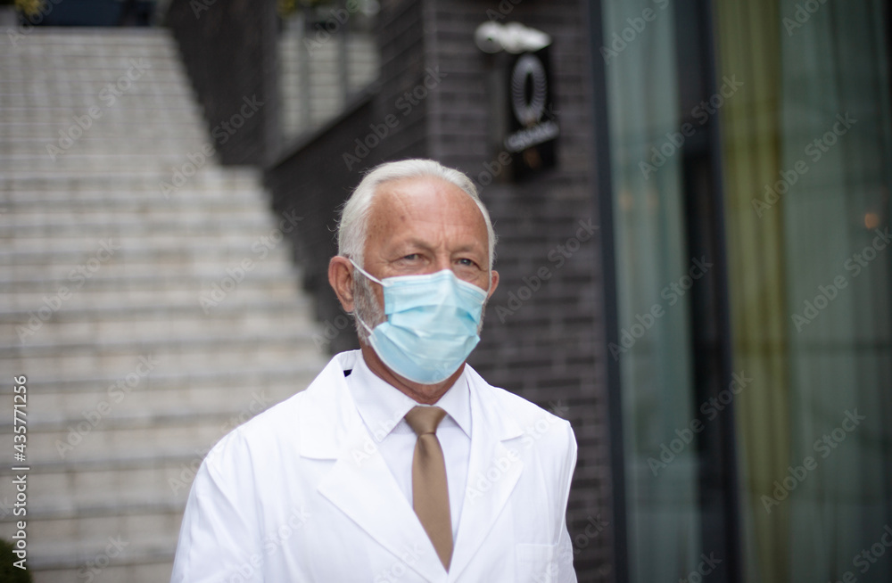 Mature serious doctor on street wearing protective mask.