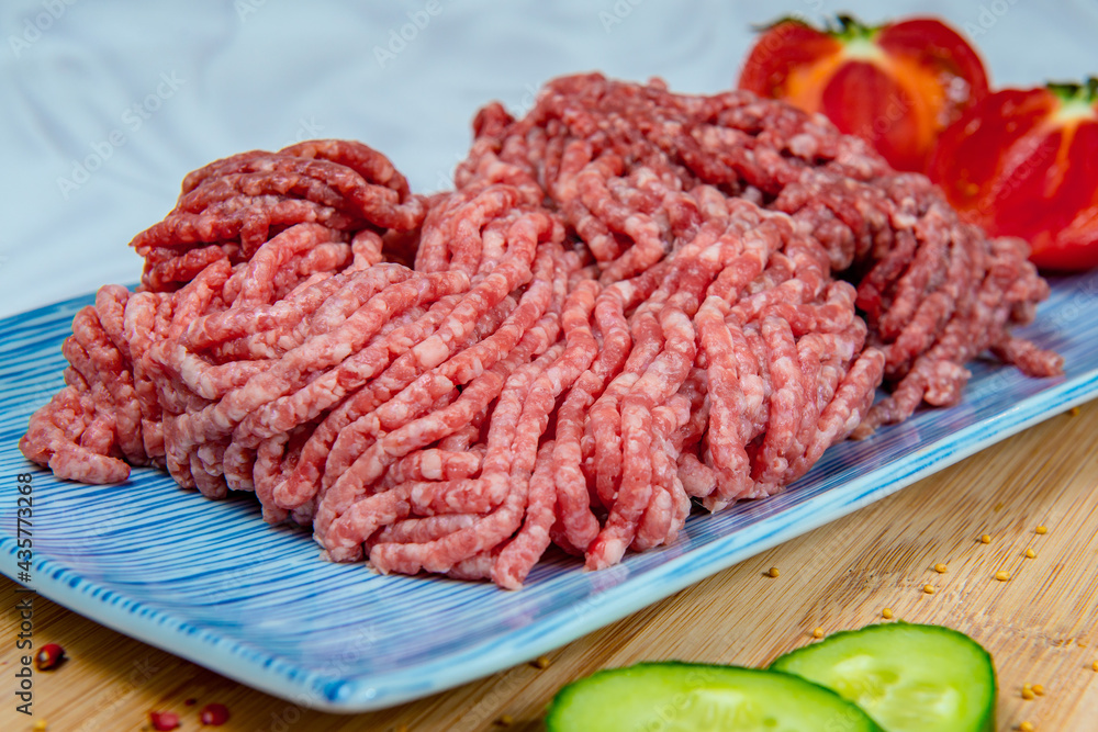 Freshly prepared ground beef in a rectangular blue plate with tomatoes and cucumbers aside Freshly prepared ground beef in a rectangular blue plate with tomatoes and cucumbers aside