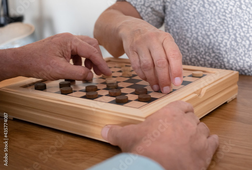 Two senior people at home while playing a game of checkers on wooden table.