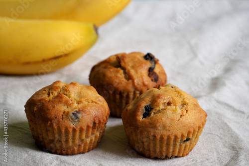 three vegan gluten-free banana muffins stand on a beige background next to yellow bananas, side view. homemade diet without lactose, eggs, gluten