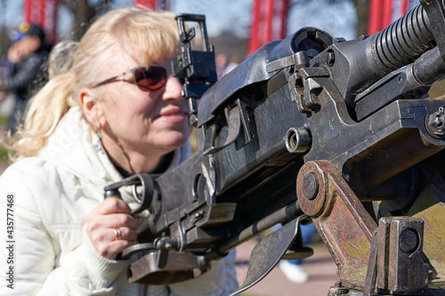 blonde woman in dark glasses shoots an anti-aircraft machine gun aiming upwards photo