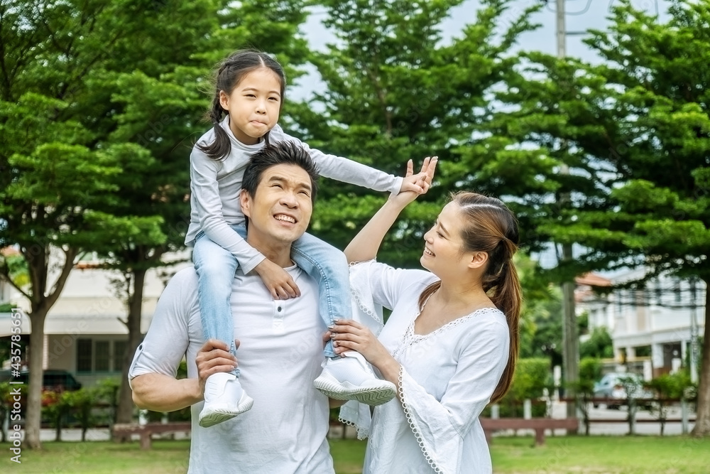 Portrait of asian happy family of three having fun together in park, little daughter sitting on father back and mother smile walking and having fun moments good time in summer park at home. Portrait of asian happy family of three having fun together in park, little daughter sitting on father back and mother smile walking and having fun moments good time in summer park at home.