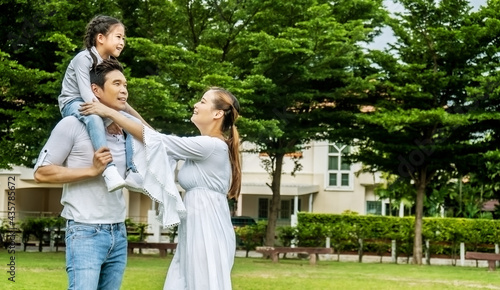 Portrait of asian happy family of three having fun together in park, father and mother holding little daughter sitting on father back walking and having fun moments good time in summer park at home