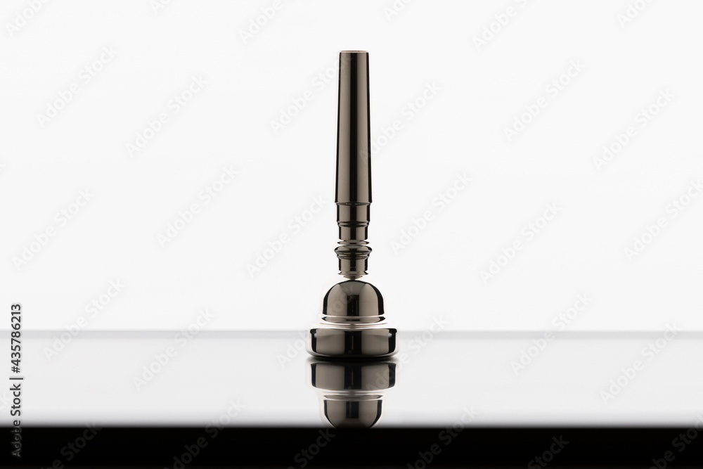 A trumpet mouthpiece on a reflective surface with a white background