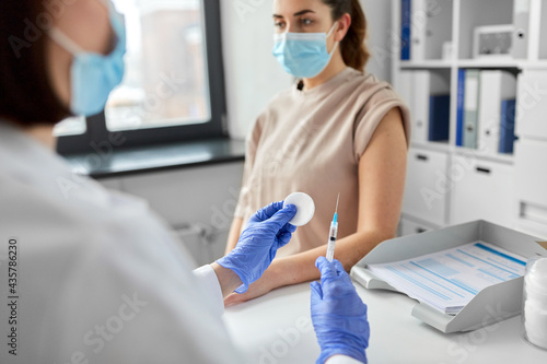 health, medicine and pandemic concept - close up of female doctor or nurse wearing protective medical mask and gloves with syringe vaccinating patient at hospital