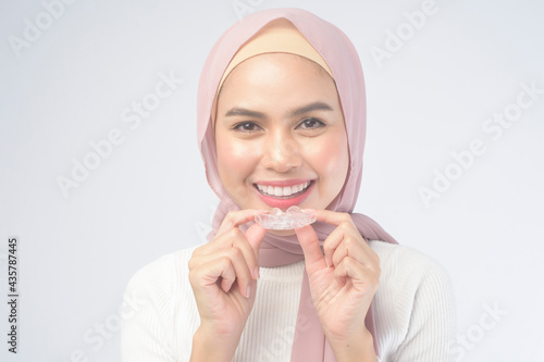 Young muslim woman holding invisalign braces over white background studio, dental healthcare and Orthodontic concept.