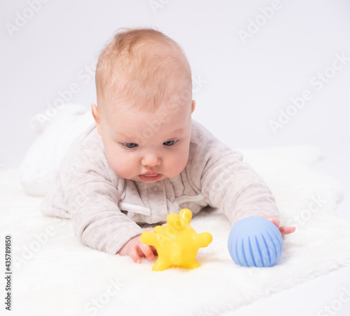 Pretty baby plays on the floor with a toy, white background