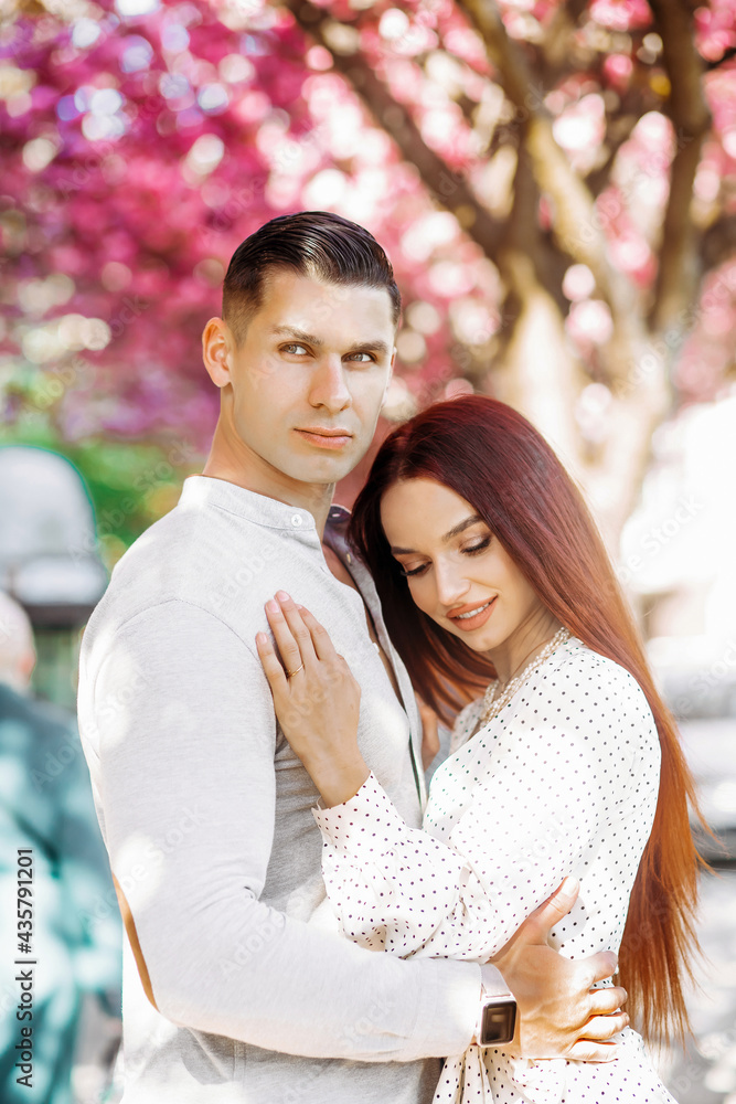 Fototapeta premium Couple in love cuddling outdoors. Romantic season.Tender love. Couple sakura tree background. Man and pretty woman enjoying pink cherry blossom.