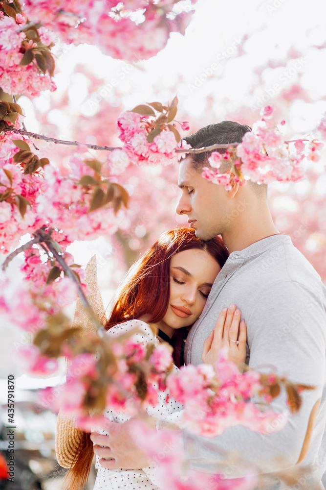Fototapeta premium Spring romantic couple in love. Sensual couple in cherry sakura blossoms flowers. The woman with her eyes closed put her head on the man's chest.