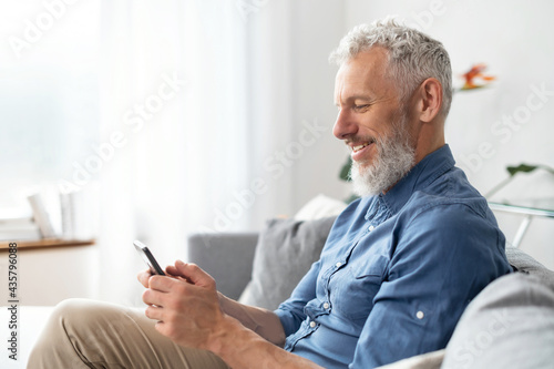 Grey-haired middle aged hipster man in casual shirt using smartphone sitting on Fototapet