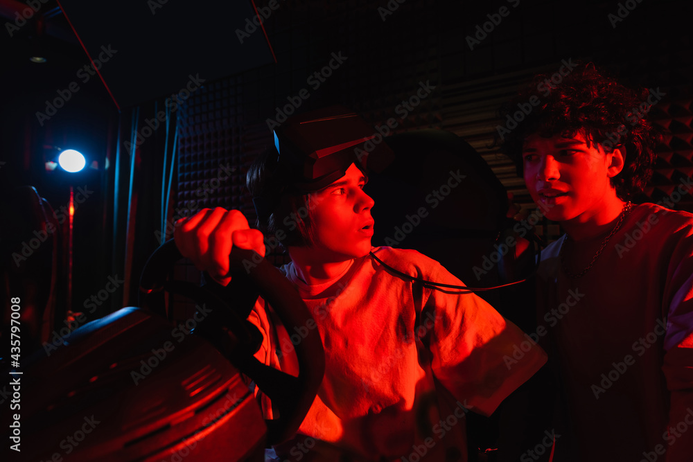 surprised boy on car simulator looking at friend in vr game zone surprised boy on car simulator looking at friend in vr game zone