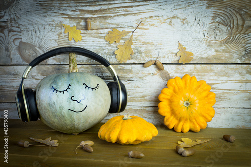 Pumpkin music lover with a funny face in headphones on a wooden background with autumn leaves. The concept of celebrating Halloween and loving music.