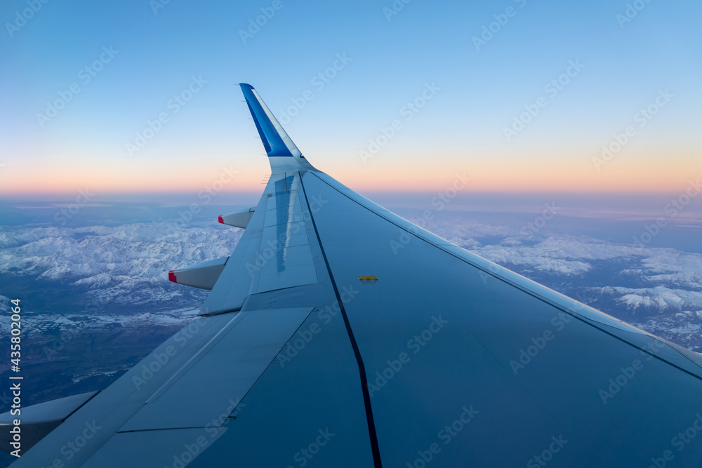 Airplane wing in flight over the Alps in winter at sunset, travel concept
