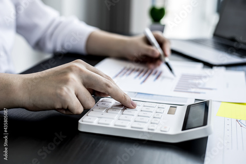 Close-up of woman holding a pen and pressing a white calculator, a corporate finance auditor examining the numbers on financial documents prepared by the finance department to bring to the meeting. © kamiphotos