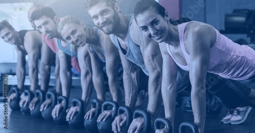 Composition of fit smiling men and women doing push ups on kettlebells in gym