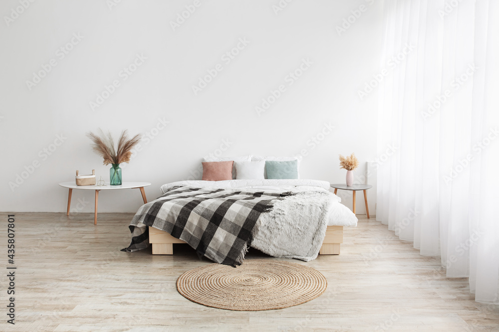 Bed with pillows and blanket, round carpet, tables with dry plants in vases  on wooden floor Stock Photo | Adobe Stock