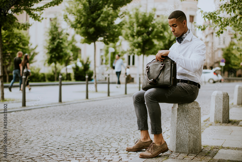 Young African American businessman using a mobile phone while waitng for a taxi on a street