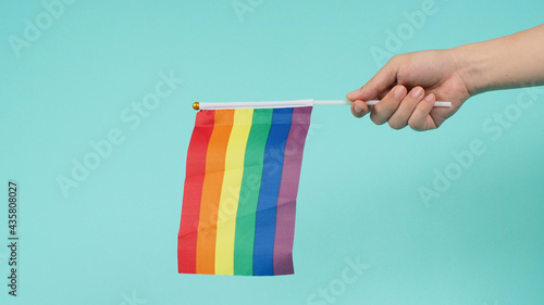 LGBT concept.Hand is holding a rainbow flag or gay flag on mint green or tiffany blue background.