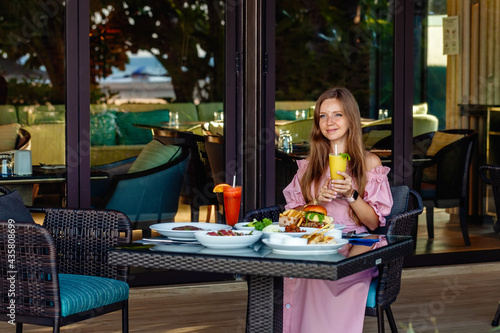 Woman Having Breakfast Relaxing Drinking Fresh Juice in Luxury Resort. Happy Tourist Enjoying Food in Outdoor Restaurant. Young Travel Woman in Dress with Cocktail Enjoy Her Dinner in Modern Cafe © TravelMedia