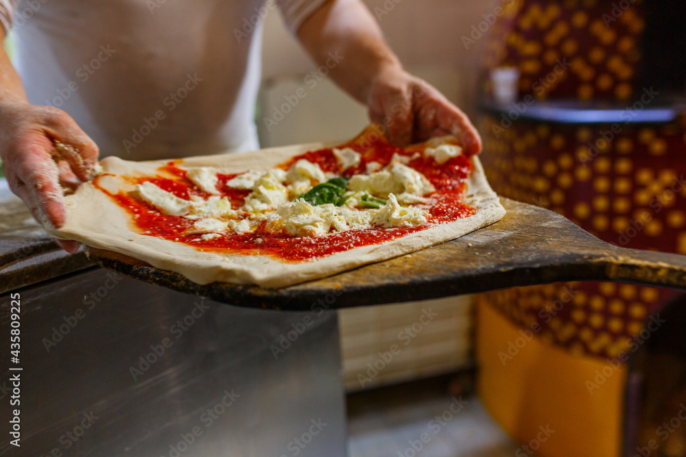 Pizza margherita napoletana con sugo di pomodoro, mozzarella di bufala e basilico mentre viene stesa su una pala di legno da forno